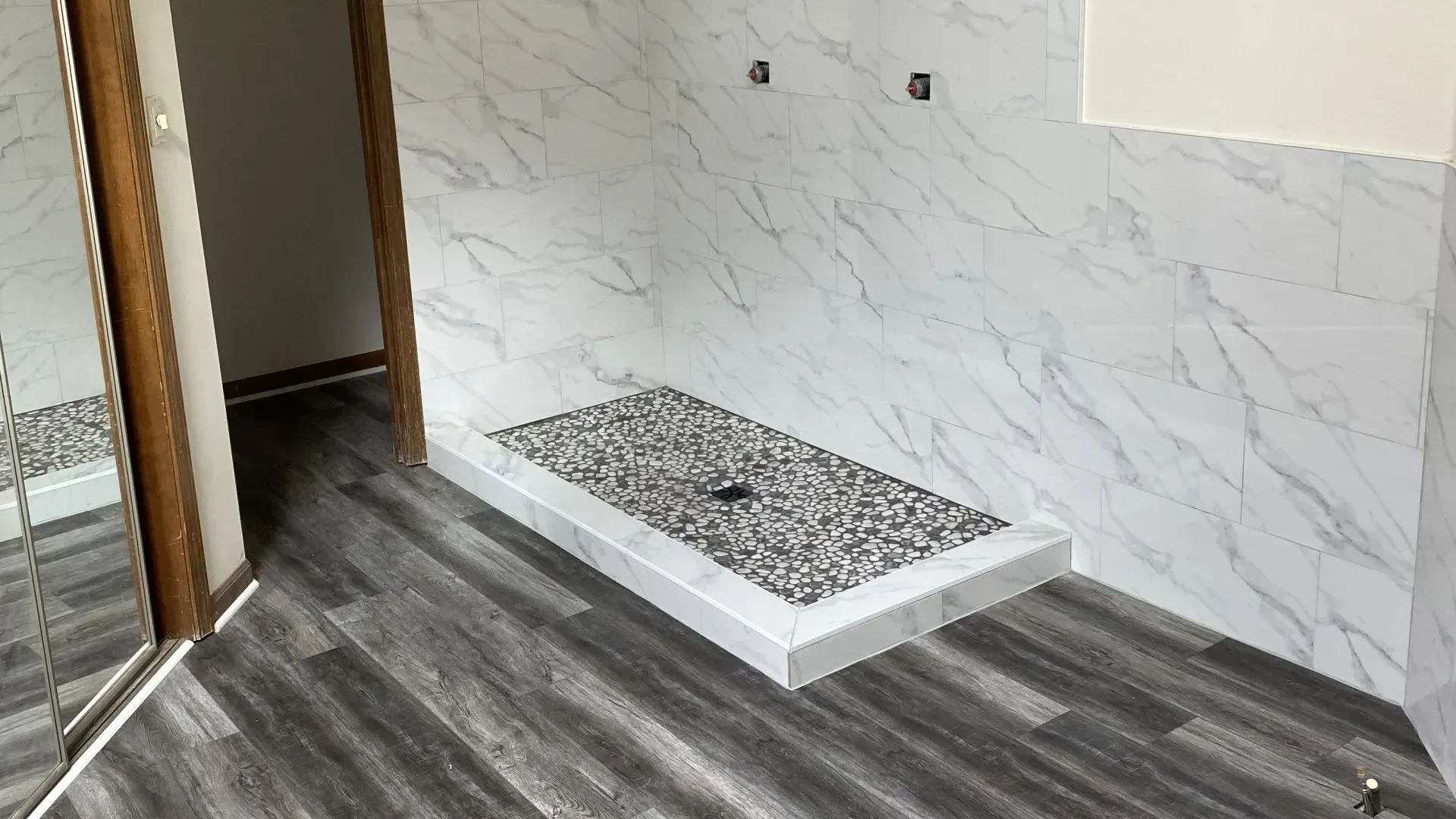 Bathroom with gray and white tile, gray wood-look flooring, and a stone-tiled shower base.