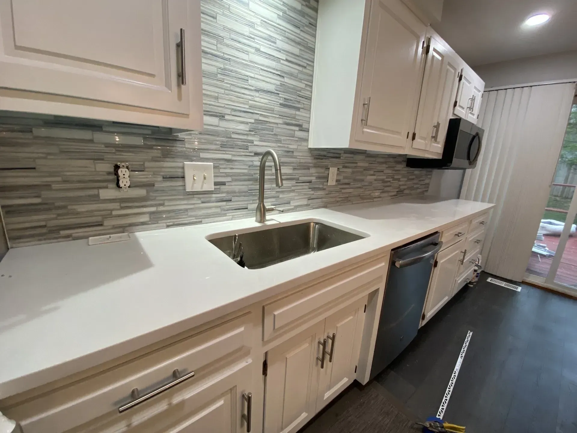 White kitchen with light countertops, stainless steel sink, and gray tile backsplash.