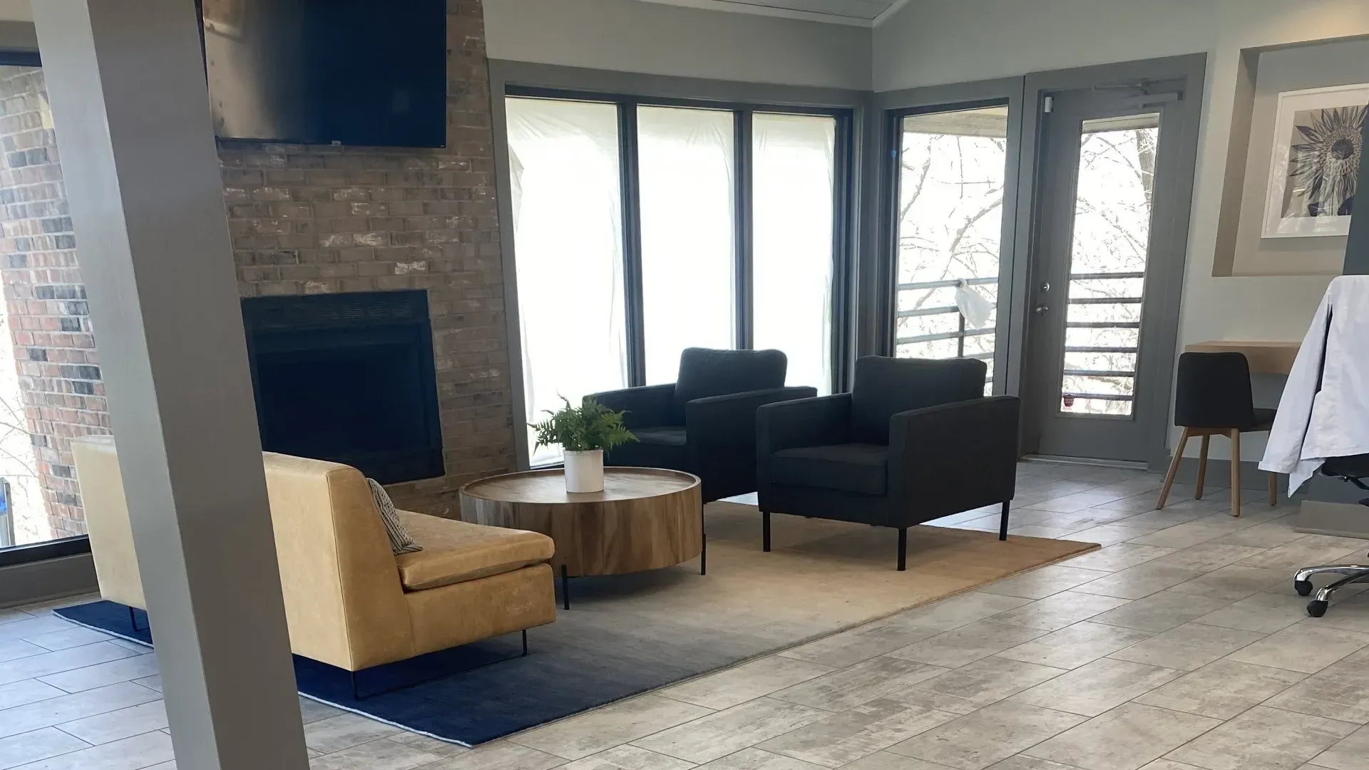 Modern living room with a fireplace, chairs, rug, and large windows.