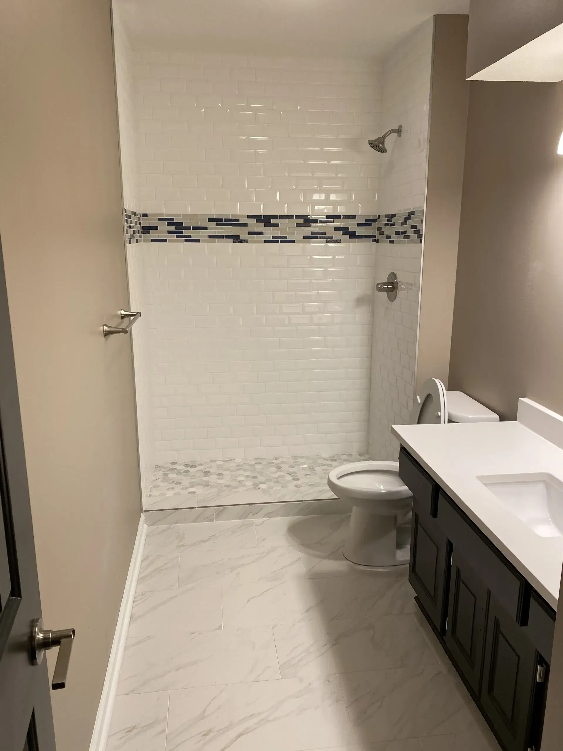 Bathroom with white tiled shower, dark vanity, and beige walls.