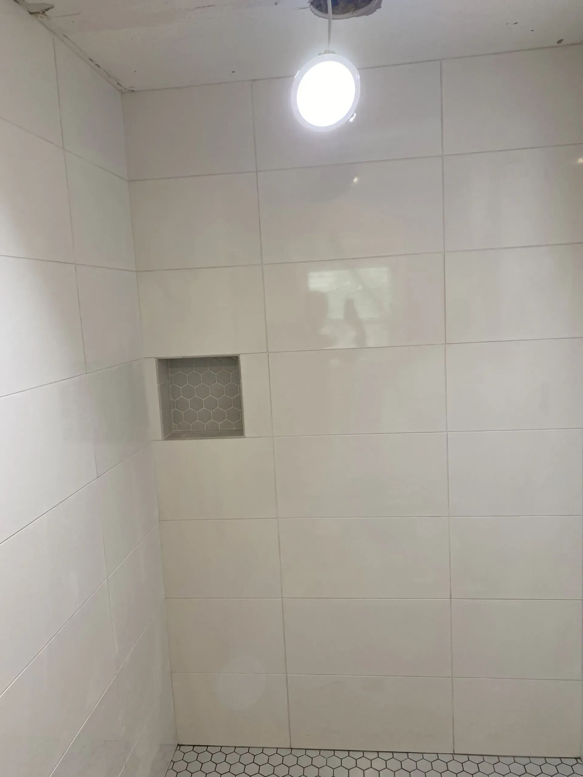 White tiled shower with a recessed shelf and overhead light.
