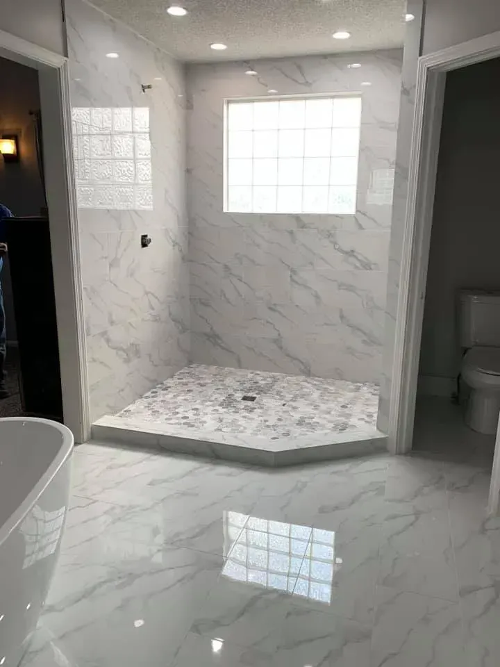 Marble-tiled bathroom with a walk-in shower. A glass block window is above the shower. A toilet and tub are also visible.