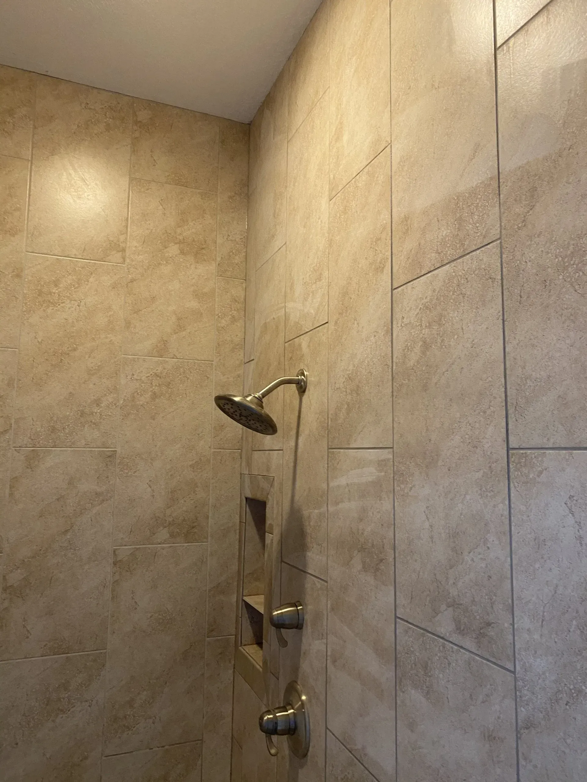 Beige tiled shower with silver showerhead and controls; recessed shelving.