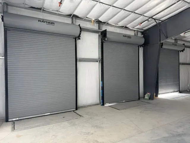 Industrial warehouse interior with three closed gray roll-up doors and concrete floor