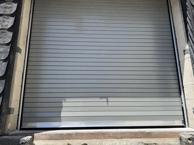 Closed gray metal roll-up door in a stone doorway with a white panel at the bottom