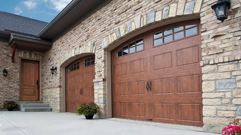 Brick house with three wooden garage doors and a front entry under a stone facade