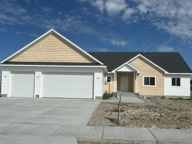 Suburban house with three-car garage, beige siding, and a wide concrete driveway under a blue sky