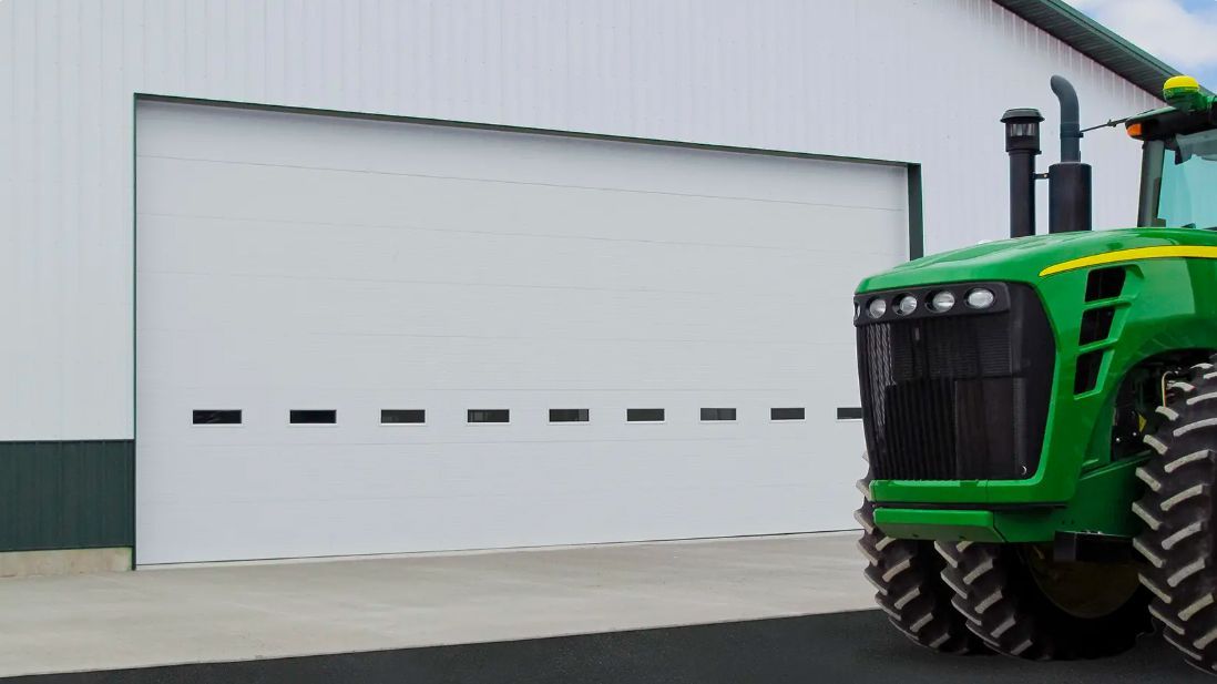 Green tractor beside a white garage door on a farm building