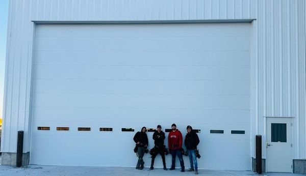 Five people stand in front of a large white warehouse door with a small side entrance.