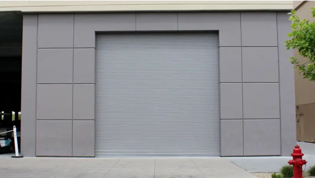 Gray garage with a closed roll-up door on a building exterior, with a red fire hydrant at right.