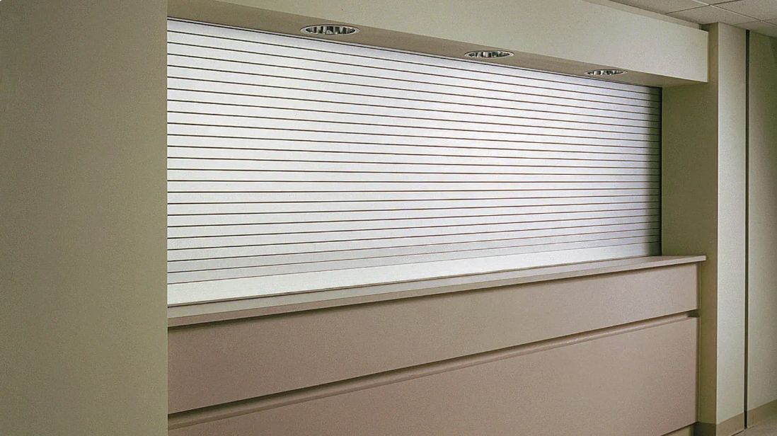 Office window with white blinds partially raised above a beige partition wall