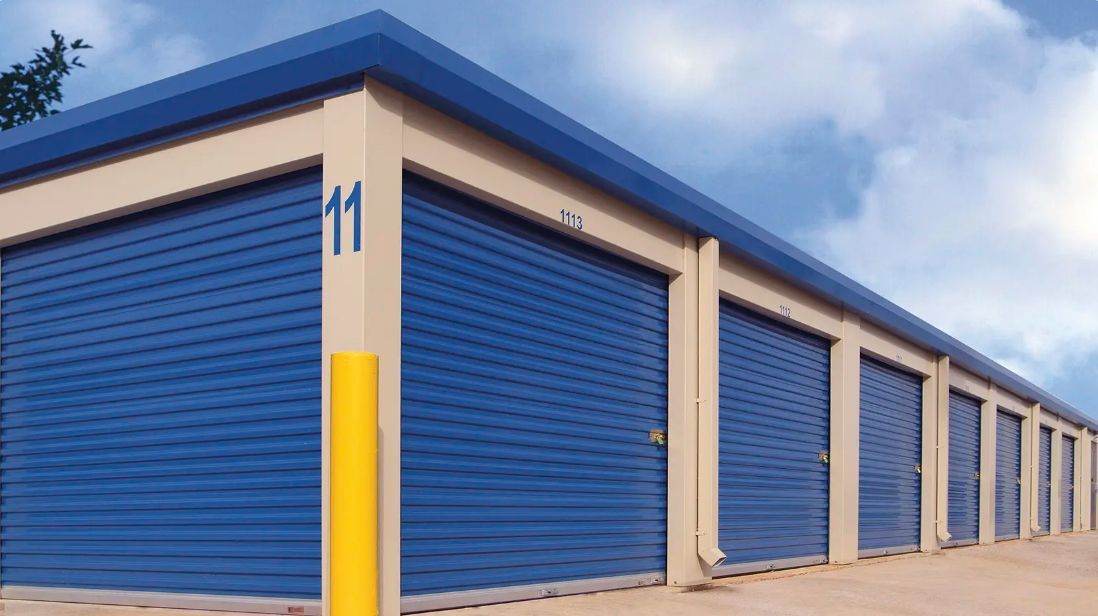 Row of blue roll-up storage unit doors in a beige building under a partly cloudy sky