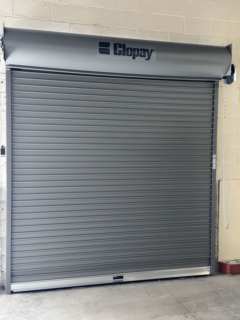 Closed gray metal roll-up door in a beige brick wall with a logo above it