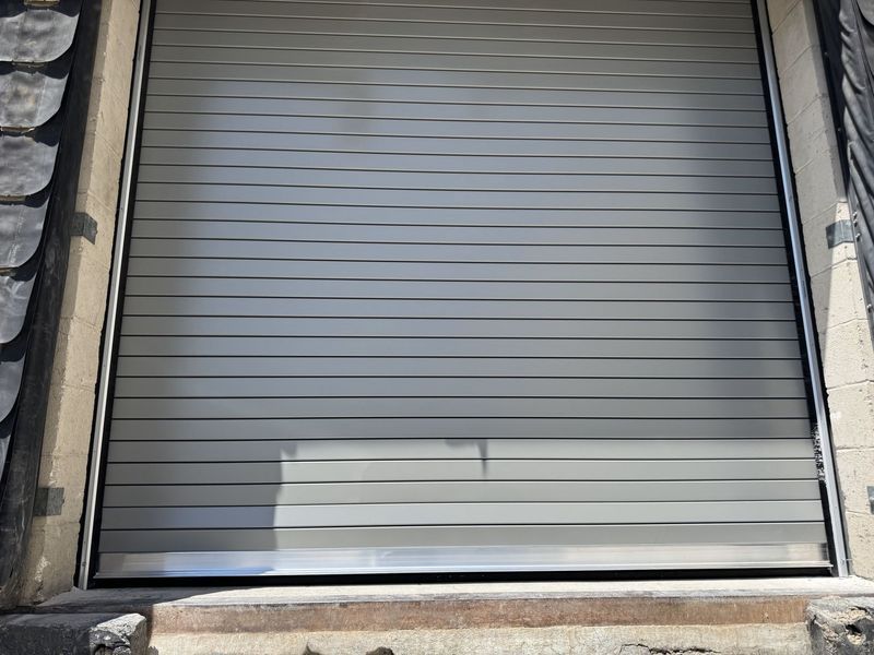 Closed gray metal roll-up garage door with a stone frame and a lighter panel near the bottom