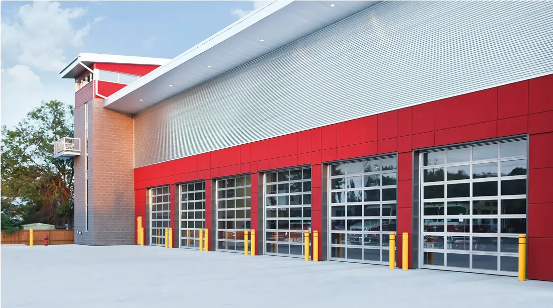 Modern red-and-gray commercial building with multiple glass garage doors and yellow bollards