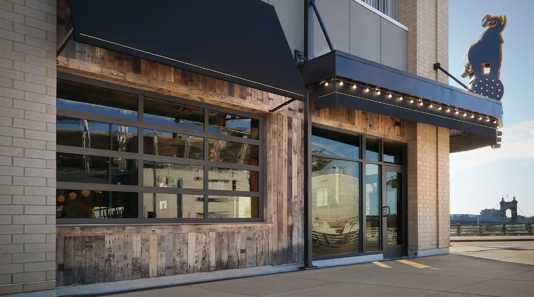 Modern storefront with glass windows, wood siding, and a lit awning at dusk