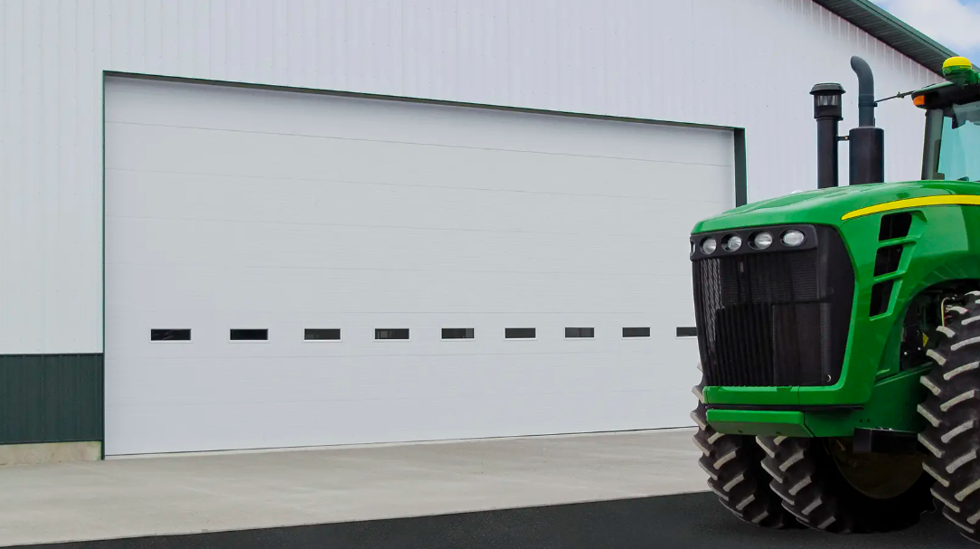 Green tractor parked beside a white garage door with small black windows.