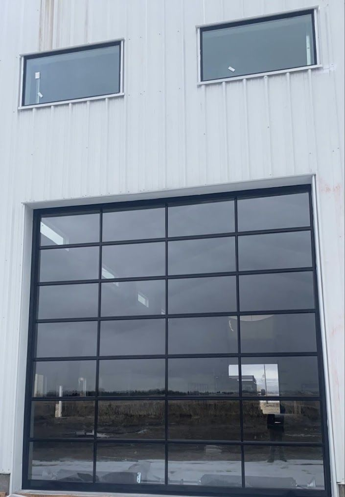 Industrial building facade with two small upper windows and a large black-framed glass garage door