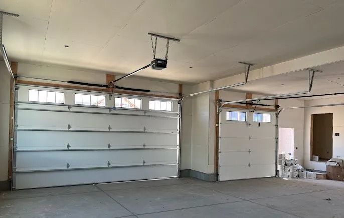 Empty garage interior with white walls, shelves, and a closed garage door under construction lighting