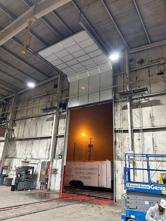 Industrial warehouse bay with a large open loading door at night, lit by overhead lights.