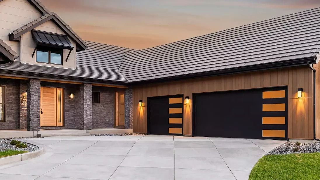 Modern house exterior with stone accents, dark garage doors, and a tiled roof at dusk