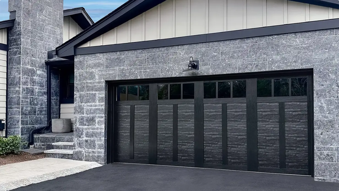 Modern house exterior with dark garage doors, stone columns, and gray siding