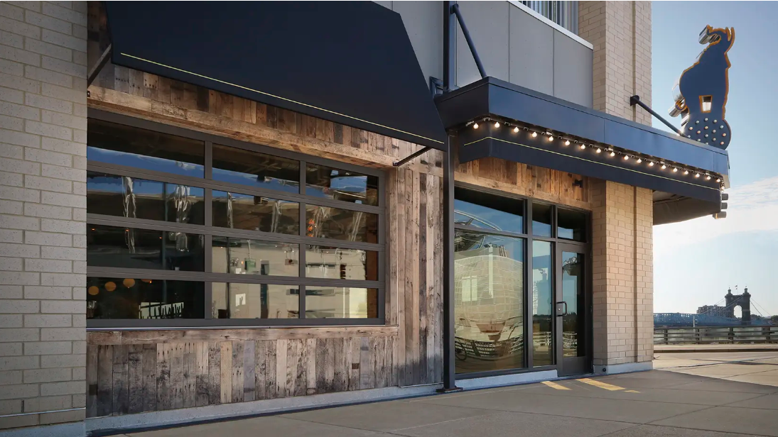 Street-facing storefront with large windows, a black awning, weathered wood siding, and a dog statue on the roof.