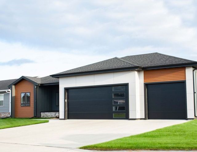 Modern suburban house with a dark gray roof, black garage doors, and a bright green lawn