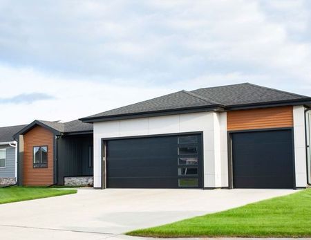 Modern suburban house with a dark gray roof, black garage doors, and a bright green lawn