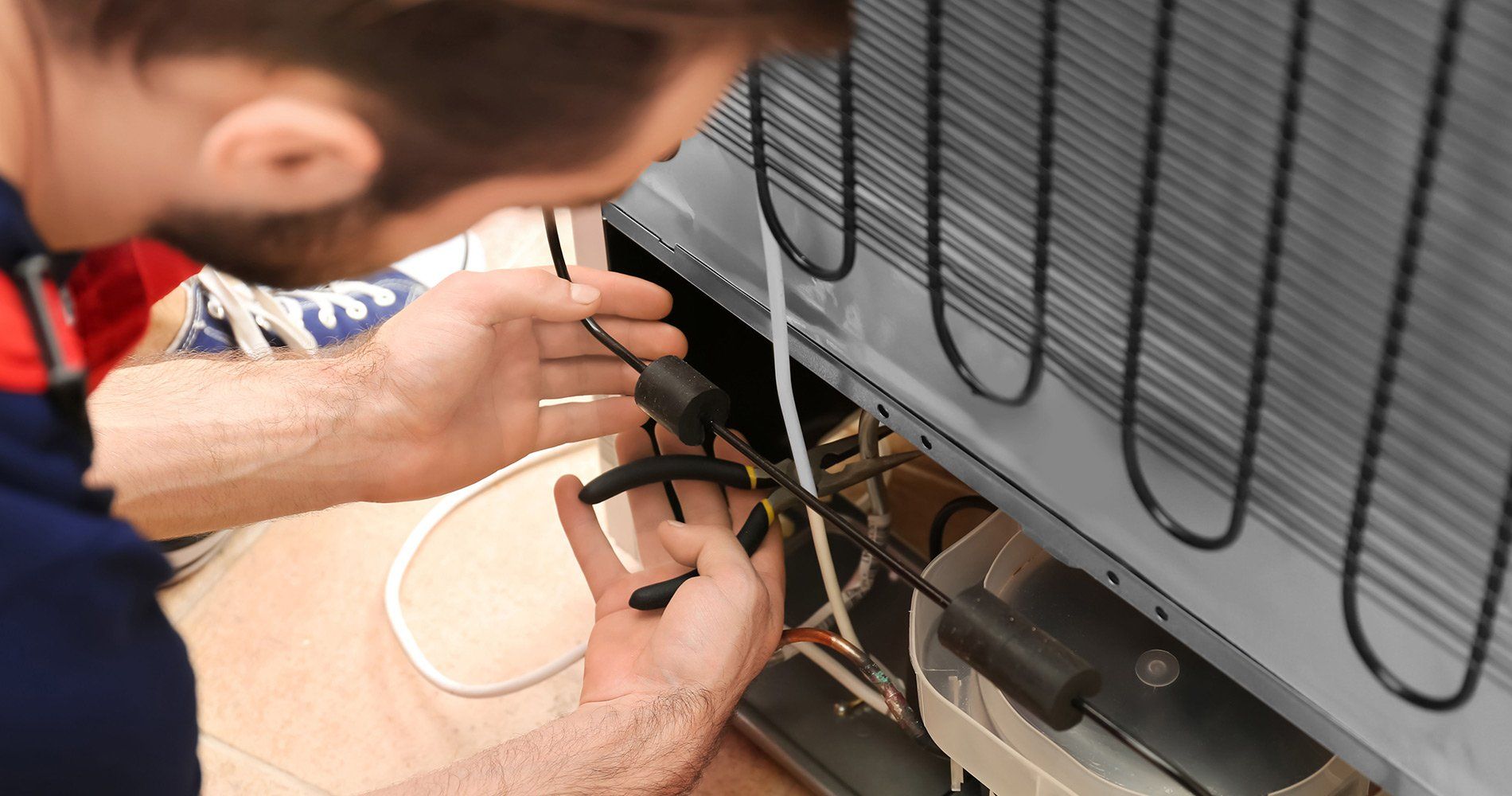 A man is repairing a refrigerator's compressor. He's working on the back of the appliance.