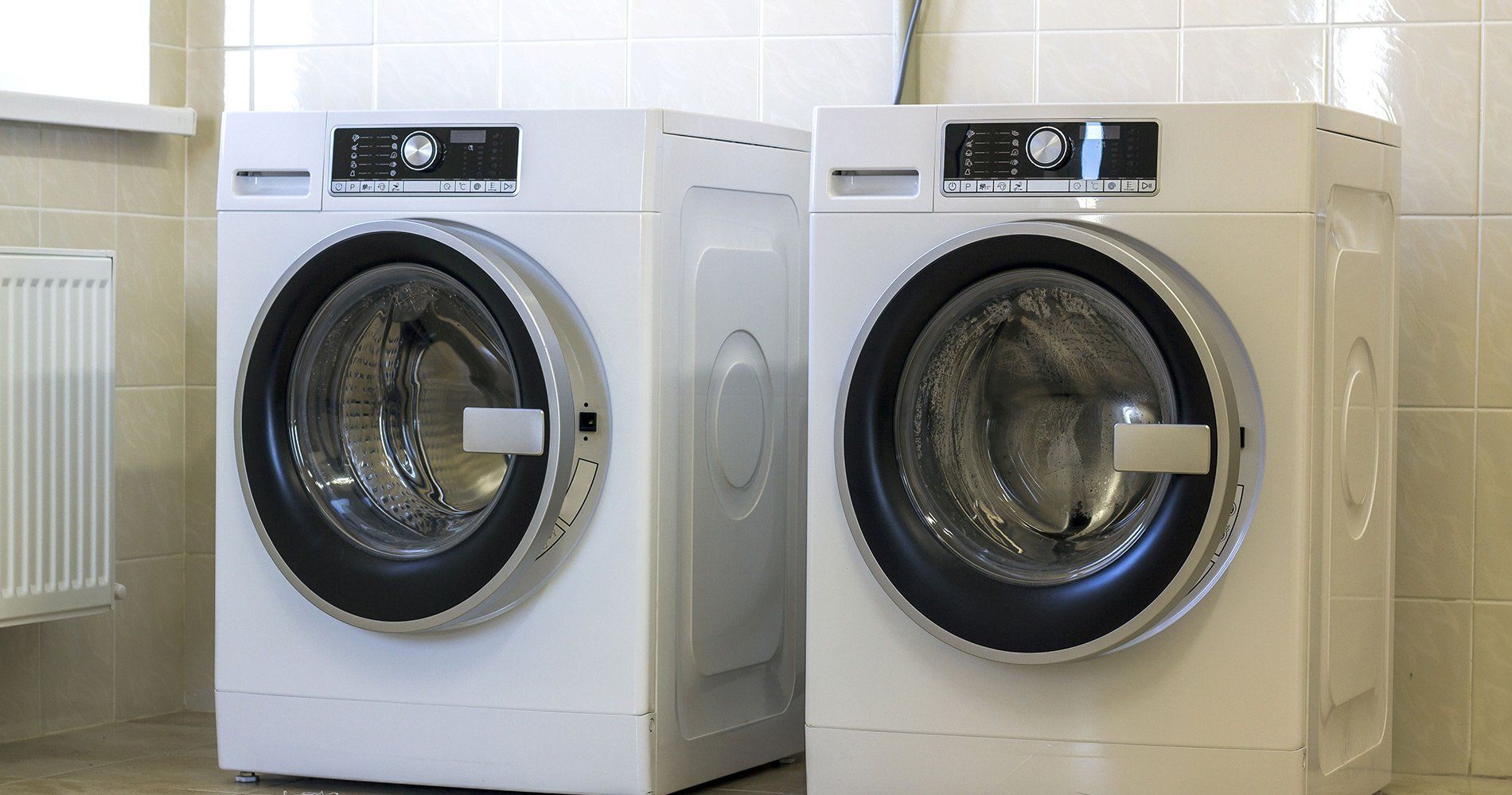 Two white washing machines side by side in a laundry room.