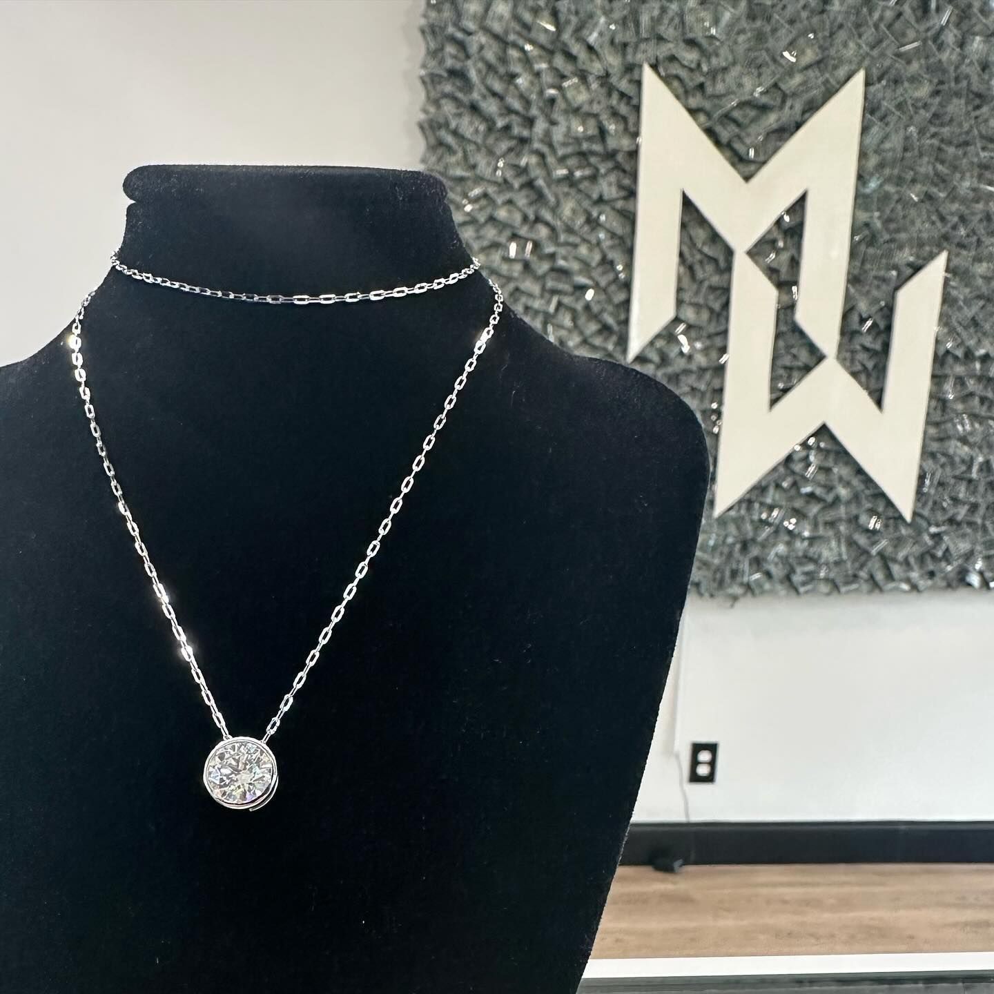 Black mannequin wearing a silver necklace with round pendant beside a geometric wall sign