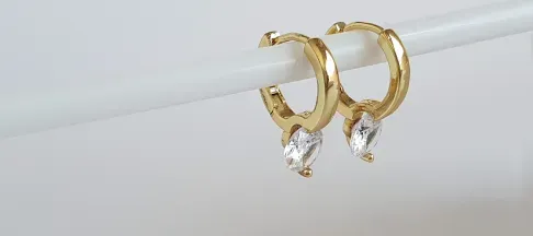 Gold hoop earrings with teardrop crystals hanging on a white rod