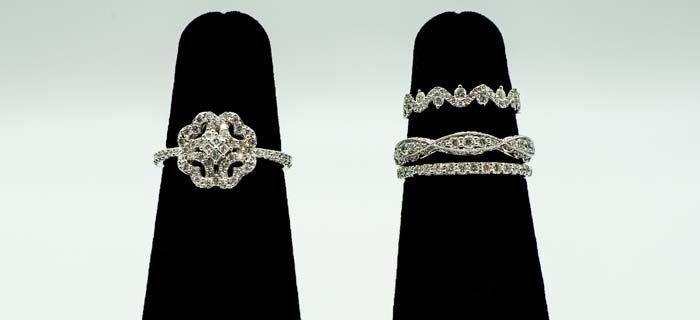 Two silver rings on black display stands, one ornate center ring and one with stacked bands