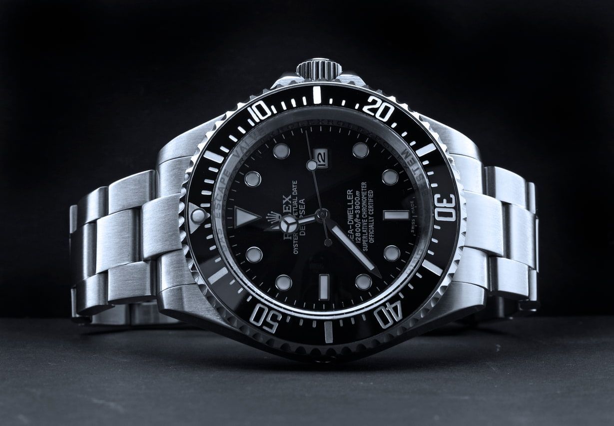 Silver wristwatch with black dial and bezel on a dark background