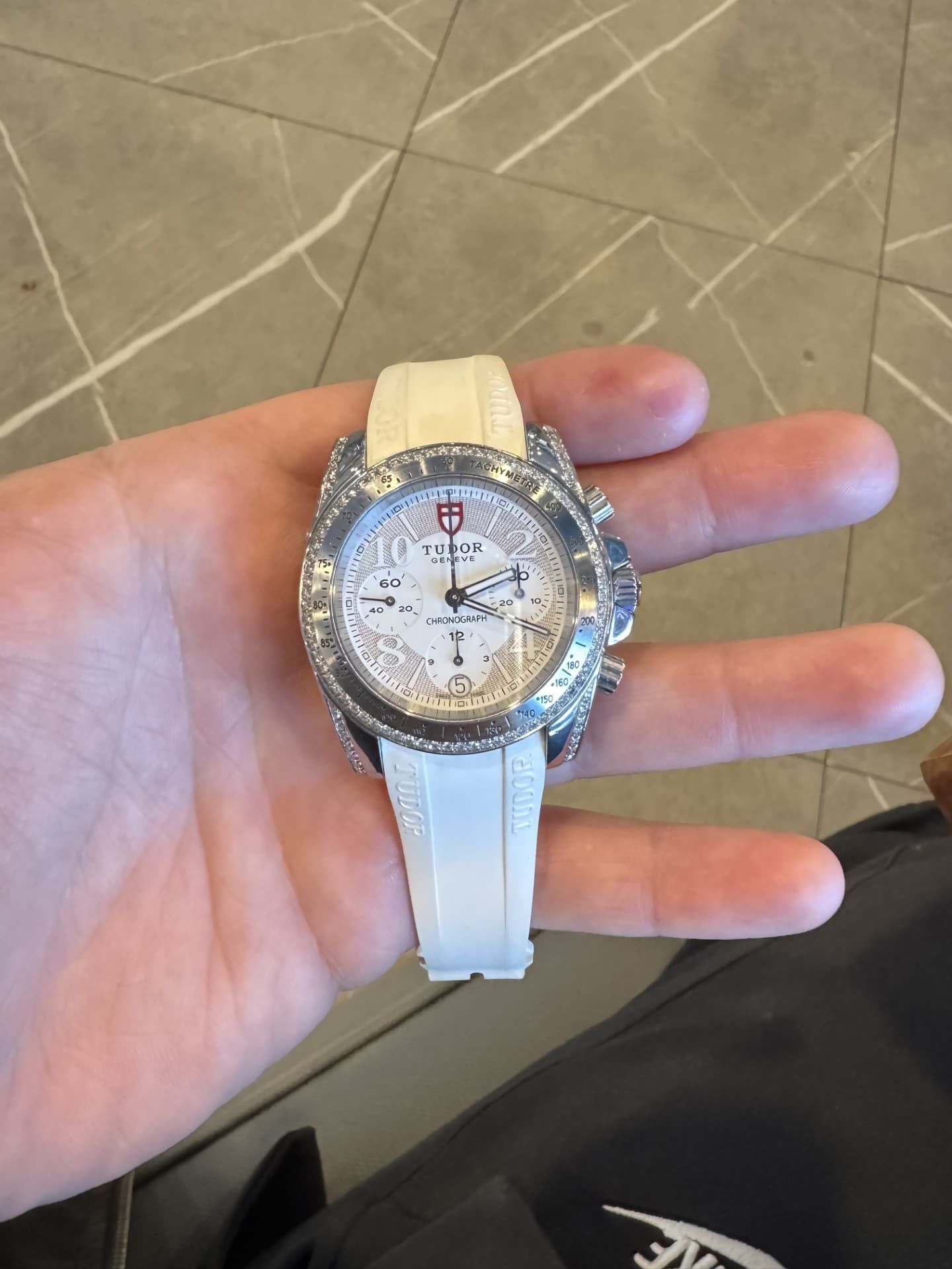 Hand holding a white wristwatch with a silver bezel over a tiled floor
