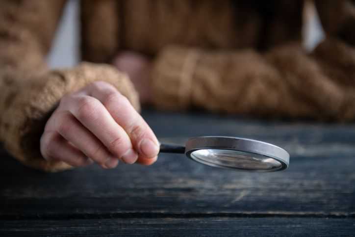 Hand holding a magnifying glass over a dark wooden surface