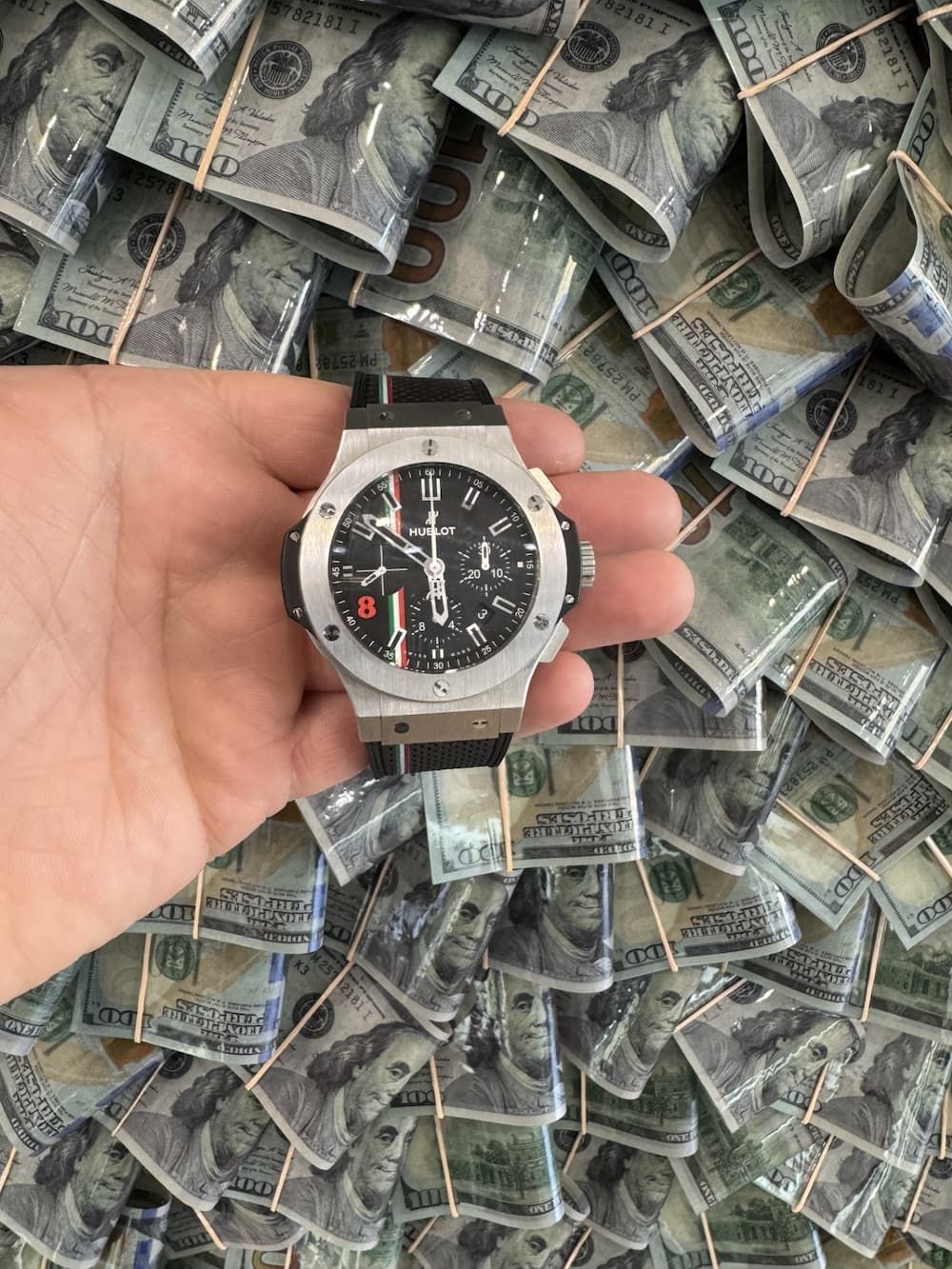 Hand holding a silver watch over a pile of cash bills