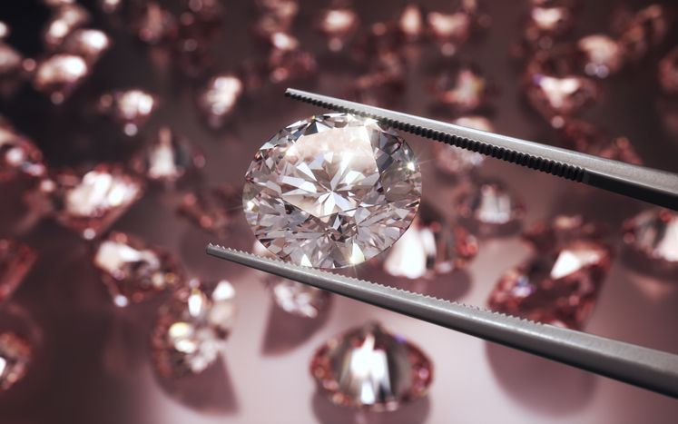 Diamond held by tweezers over scattered gemstones on a dark pink background