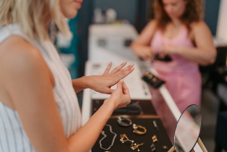 Person trying on rings at a jewelry counter while another person stands in the background