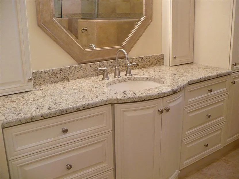 Bathroom vanity with white cabinets, granite countertop, oval sink, and octagonal mirror.