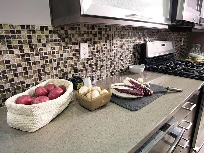 Kitchen countertop with fresh produce, backsplash, and stovetop.
