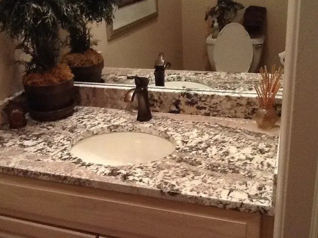 Bathroom vanity with granite countertop, oval sink, dark faucet, and potted plant.