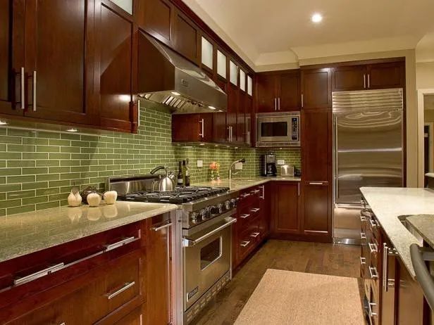 Dark wood kitchen with green tile backsplash, stainless steel appliances, and beige countertops.