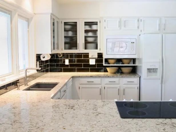 White kitchen with granite countertops, stainless steel sink, and black backsplash.