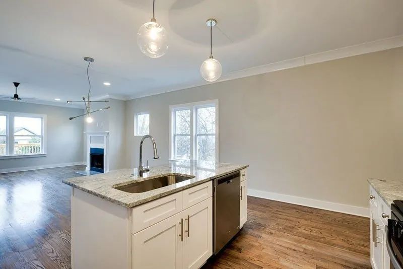 Kitchen with white cabinets, island sink, and pendant lights; hardwood floors.