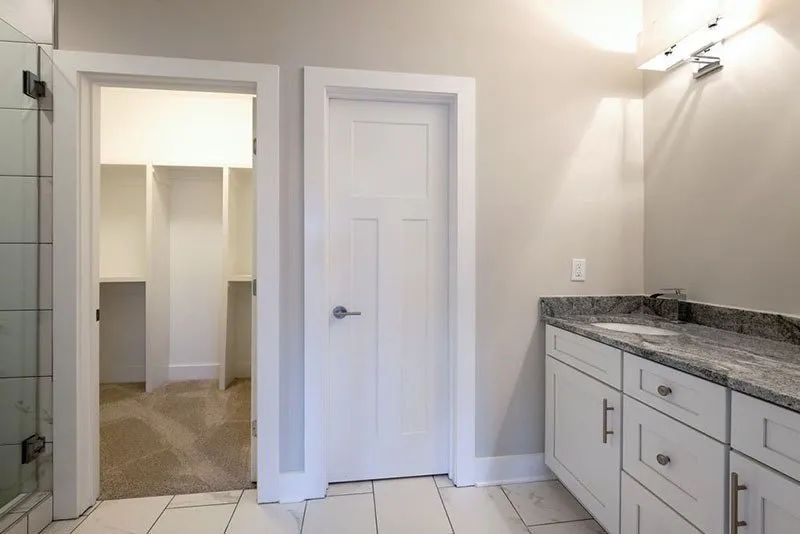 Bathroom with white cabinets, marble countertop, and a walk-in closet in the background.