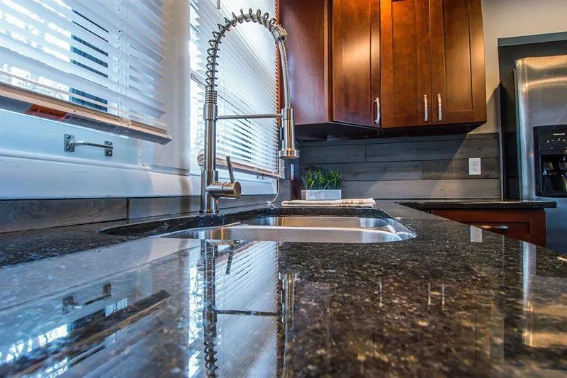 Kitchen with granite countertop, stainless steel sink and faucet, wooden cabinets, and blinds.