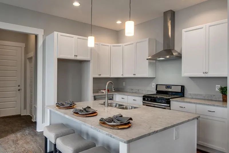 Modern white kitchen with island, gray countertops, and stainless steel appliances.
