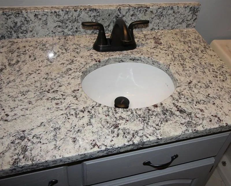Bathroom vanity with a white oval sink, granite countertop, and gray cabinet with black hardware.